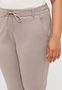 Nahaufnahme von der Taille einer Person, die hellgraue Hosen mit elastischem Bund und Kordelzug trägt, wobei Hand- und Taschen-Details hervorgehoben werden.