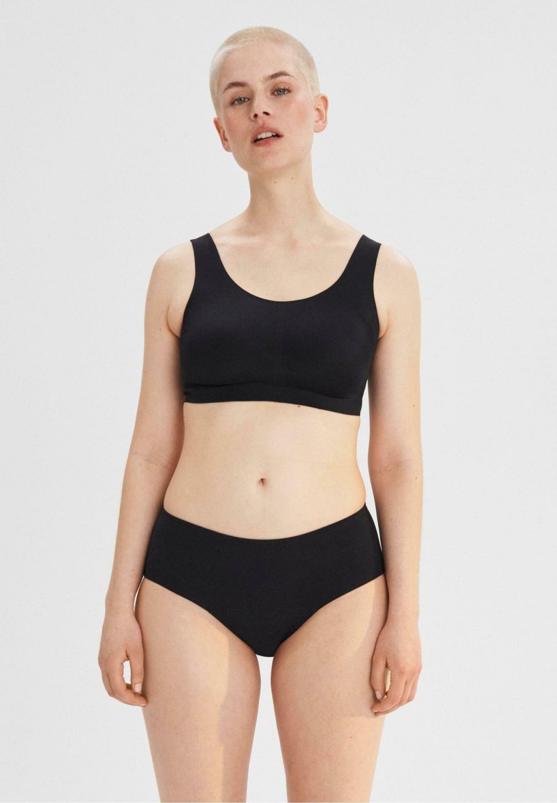 Musta saumaton bralette leveillä olkaimilla ja sileällä pinnalla, yhdistettynä korkeavyötäröisiin mustiin bikinitutiloihin. Molemmilla vaatteilla on minimalistinen muotoilu.