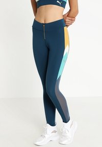 Marinblå träningsleggings med meshpaneler, geometriska detaljer i turkos och orange, samt en zipplås framtida ficka. Tillverkade av ett stretchigt material.