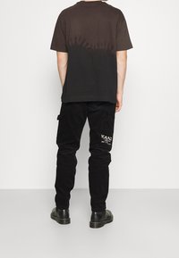 Czarny t-shirt z gradientowym wzorem przechodzącym z czerni na ciemnoszary na plecach, w połączeniu z czarnymi spodniami sztruksowymi z logo.