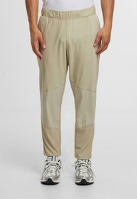 Jasno beżowe spodnie sportowe o teksturowanym wykończeniu, z elastycznym pasem, bocznymi kieszeniami oraz kontrastowym wzorem na panelach.