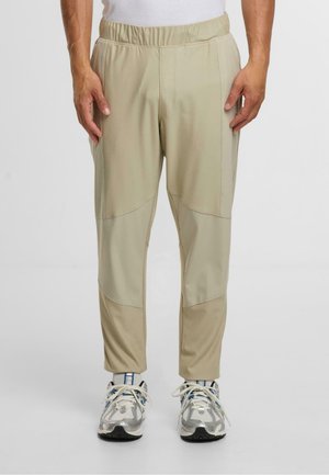 Jasno beżowe spodnie sportowe o teksturowanym wykończeniu, z elastycznym pasem, bocznymi kieszeniami oraz kontrastowym wzorem na panelach.