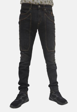 Jeans in denim nero con una vestibilità slim, dotati di tasche applicate doppie e cuciture arancioni a contrasto. Indossati con scarpe sportive nere.