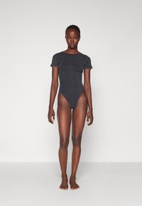 Svart stripete bodysuit med korte ermer, høy benkutt og tettsittende design. Myk tekstur mot nøytral bakgrunn.
