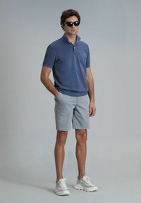 Dunkelblaues Baumwoll-Polohemd mit Kragen und kurzen Ärmeln, kombiniert mit hellgrauen Shorts. Weiße Sneakers für den Sport und schwarze Sonnenbrille.