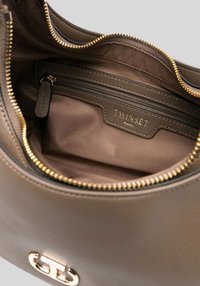 Interieur van een bruine leren handtas met een ritsvak, gouden ritsafwerking en een lichtbruine stoffen voering. Merken zichtbaar aan de binnenkant.