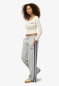 Lichtbeige langamige top met een henley halslijn en marineblauwe letters. Grijze sweatpants met zijzakken en marineblauwe strepen. Bruine sneakers.