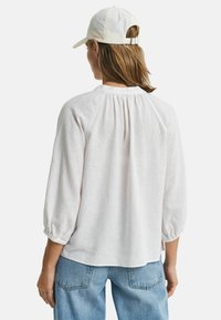 Lichte, crème-kleurige linnen blouse met driekwart pofmouwen en een gathered achterkant. Gecombineerd met blauwe denim jeans.