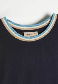 Granatowy t-shirt z prążkowanym okrągłym dekoltem, z jasnoniebieskimi, beżowymi i białymi paskami. Metka głosi "diverse" oraz rozmiar "M". Gładka faktura.