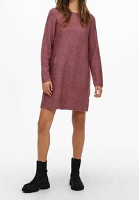 Strickkleid in einem sanften Mauve-Ton mit geripptem Textur, ausgestattet mit einem runden Ausschnitt und langen Ärmeln, kombiniert mit schwarzen Stiefeletten.