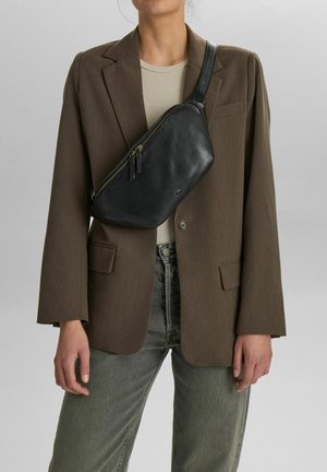 Must must nahktakott sujuva tekstuuri, veidi kõver kuju ja kahe tõmblukuga. Kantud üle keha beeži särgi ja bleizeri peal.