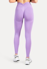 Hellviolette Leggings mit hohem Bund, mit einer gerafften Naht auf der Rückseite und elastischem, glattem Stoff. Kombiniert mit weißen Sportschuhen.