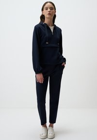 Felpa blu navy con zip a un quarto e lacci, abbinata a pantaloni aderenti coordinati. Tessuto morbido e testurizzato con polsini elasticizzati.