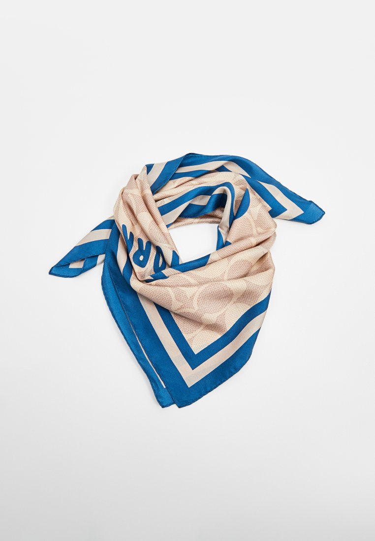 Foulard en soie présentant un motif géométrique beige et bleu, avec une bordure bleue audacieuse et des rayures plus claires. Le matériau a une texture lisse.