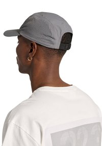 Szara perforowana czapka z zakrzywionym daszkiem i regulowanym paskiem z tyłu, zestawiona z prostą białą koszulką.