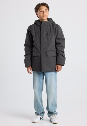 Grau isolierte Jacke mit Kapuze, ausgestattet mit einer mit Reißverschluss versehenen Brusttasche und zwei Fronttaschen; getragen über hellblauen Jeans und weißen Sneakers.