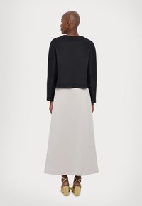 Svart cropped jakke med lange ermer, sammen med en lys grå maxiskjørt. Sandaler har en kraftig hæl og tynne ankelremmer.
