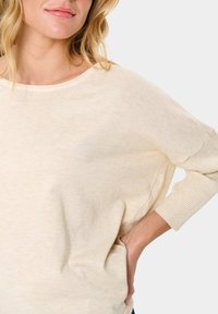 Helebeež oversize kampsun ümmarguse kaelusega ja kolmeveerandi pikkusega varrukatega. Tekstureeritud, kerge kangas ribadega mansetid.