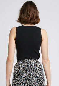 Débardeur noir à côtes avec des bords festonnés, associé à une jupe à motif floral comportant diverses couleurs sur un fond sombre.