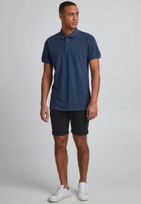 Navy polo shirt with a collar and three buttons, paired with rolled black shorts and white sneakers. Simple design, lightweight fabric.