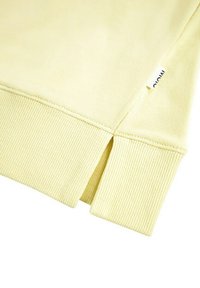Felpa gialla chiara con polsini e orlo a costine, con uno spacco laterale, texture liscia e una piccola etichetta bianca sulla cucitura.