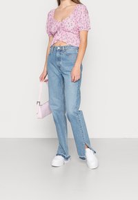 Růžový květinový crop top s nabíranými rukávy, spárovaný se sv ětle modrými džíny s vysokým pasem a bočními rozparky, doplněný bílými platformovými teniskami.