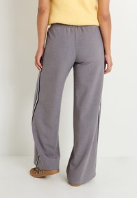 Pantalones de pierna ancha en gris claro, hechos de un tejido texturizado, con rayas laterales negras y una cintura elástica. Combinados con zapatos marrones tipo slip-on.