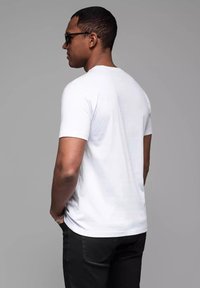 Hvid kortærmet t-shirt i bomuldsstof, rund halsudskæring, båret med sorte bukser. Modellen viser solbriller, minimalistisk design, ensfarvet.