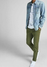 Jeansskjorta med knappar över en vit t-shirt, i kombination med olivgröna byxor och vita sneakers. Skjortan har bröstfickor och en klassisk krage.