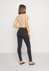 Jeans pitillo negros de cintura alta con bolsillos traseros sutiles, combinados con una camiseta ajustada beige de canalé y sandalias negras con tacón.
