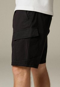 Fekete cargo short, könnyű anyagból készült, oldalzsebbel, fedéllel, egyenes szabású és enyhén texturált felülettel.