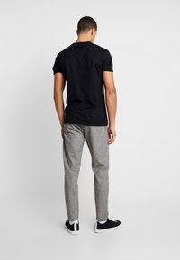T-shirt noir à manches courtes assorti à un pantalon à carreaux gris clair et des baskets foncées, présenté de dos sur un fond uni.