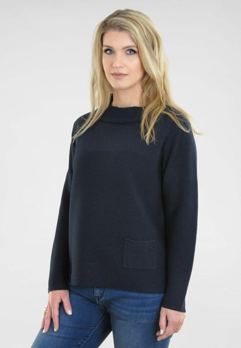 Navy trui met een ronde halslijn, ribbelstructuur, lange mouwen en een voorzak, gecombineerd met blauwe denim jeans.