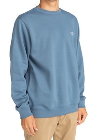 Sudadera azul clara hecha de una suave mezcla de algodón, con cuello redondo, mangas largas, puños y dobladillo acanalados, y un pequeño logo en el pecho.