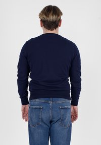 Maglione blu navy con maniche lunghe, scollo a giro e polsini a coste, abbinato a jeans in denim blu con tasche posteriori.