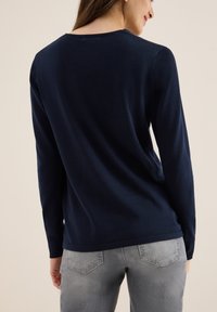 Granatowy sweter z długim rękawem, wykonany z dzianiny, z okrągłym dekoltem, gładką fakturą i minimalnymi detalami, w połączeniu z jasnoszarymi dżinsami.