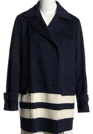 Manteau bleu marine croisé avec larges revers et deux bandes blanches horizontales près de l'ourlet, présenté sur un mannequin blanc.