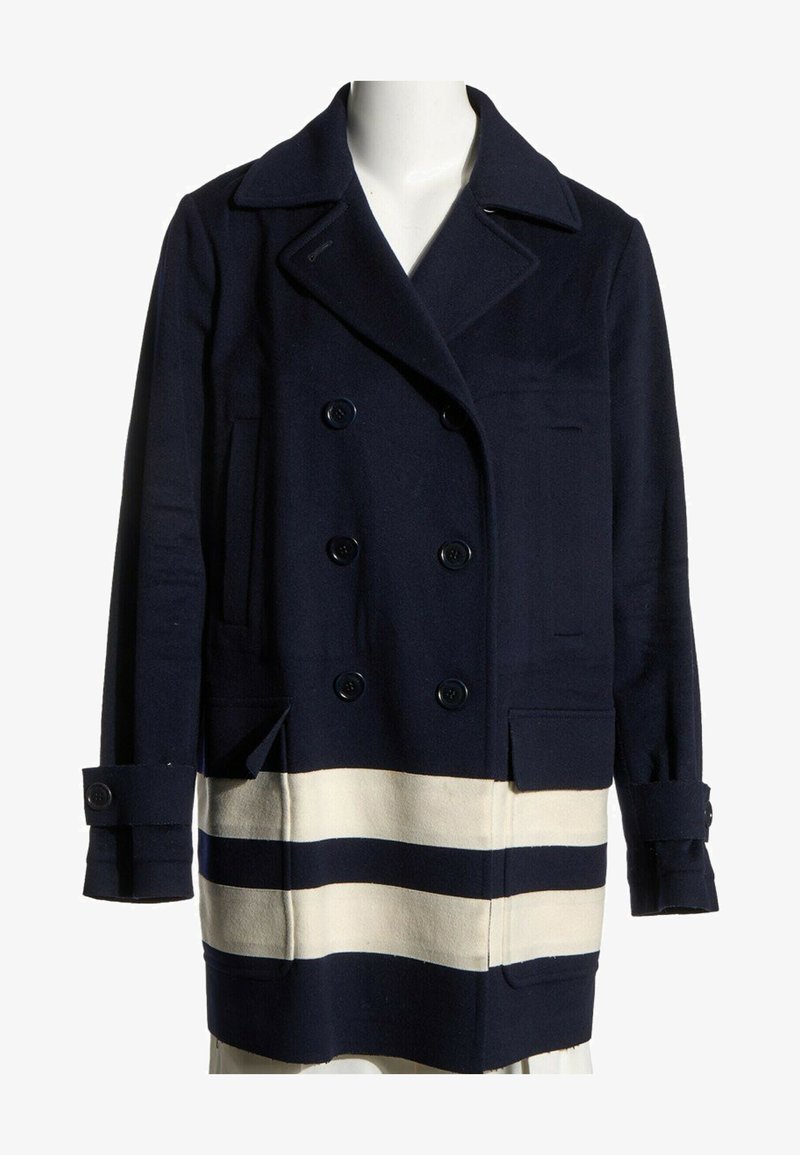 Manteau bleu marine croisé avec larges revers et deux bandes blanches horizontales près de l'ourlet, présenté sur un mannequin blanc.