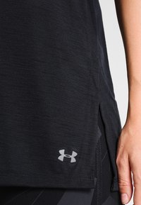 Svart atletisk tröja i textilmaterial, med en sidoklyvning och en liten vit logotyp på fållen.