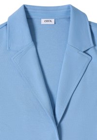 Blazer bleu clair avec revers crantés et une étiquette blanche portant l'inscription « Cecil » cousue à l'intérieur du col.