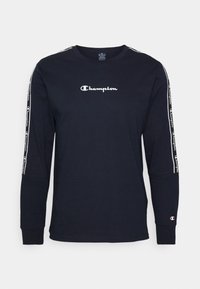 Dlouhý rukáv námořnický modrý bavlněný tričko s bílým logem Champion na hrudi a pruhy s potiskem loga podél rukávů.