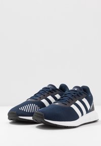 Dunkelblaue Adidas-Laufschuhe mit weißen Streifen, schwarzen Sohlen und Schnürsenkeln, nebeneinander auf einer weißen Fläche präsentiert.