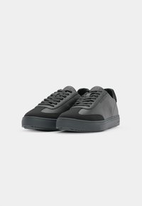 Black sneakers with a combination of smooth and textured materials. Features a rounded toe, lace-up design, and a thick rubber sole.