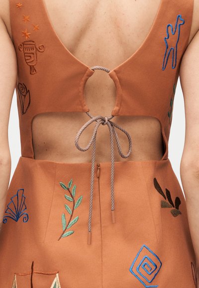 Οπίσθια όψη ενός καφέ φορέματος με κεντητά πολύχρωμα σχέδια, διαθέτοντας κυκλικό άνοιγμα και δεμένη λεπτομέρεια σχοινιού στο πάνω μέρος της πλάτης.