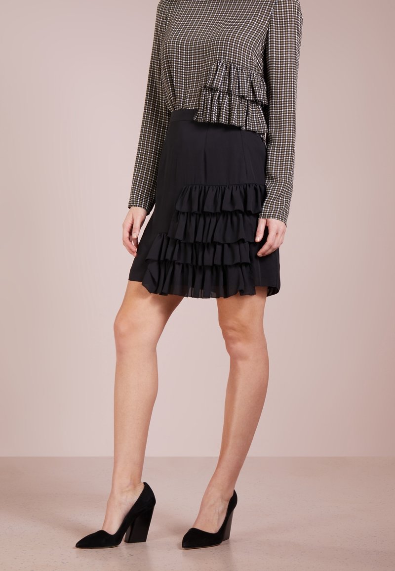 Czarna falbaniasta spódnica z warstwowej tkaniny, zestawiona z długim, w kratę topem. Do kompletu czarne zamszowe buty na wysokim obcasie.