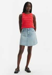 Top sans manches en crochet rouge avec des rayures horizontales, associé à une jupe en denim bleu clair. Le modèle porte des chaussures plates noires. Fond neutre.