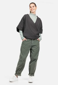 Top grigio avvolgente in tessuto morbido sopra un dolcevita verde chiaro, abbinato a pantaloni larghi verde oliva e scarpe da ginnastica bianche. Design semplice e moderno.