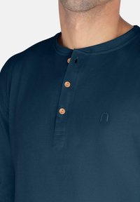Marineblaue Langarmshirt aus weichem Stoff, mit Henley-Ausschnitt, drei braunen Knöpfen und einem dezenten Logo-Detail.