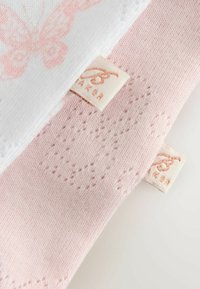 Calzini morbidi per neonati in rosa chiaro e bianco con motivi a farfalla e piccole etichette di tessuto del marchio attaccate, su una superficie bianca.