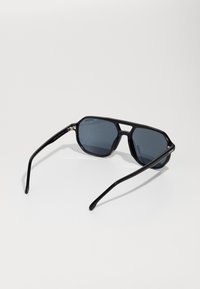 Ochelari de soare negri cu rame unghiulare și lentile întunecate. Au brațe elegante cu un finisaj strălucitor și un logo mic pe ramă.